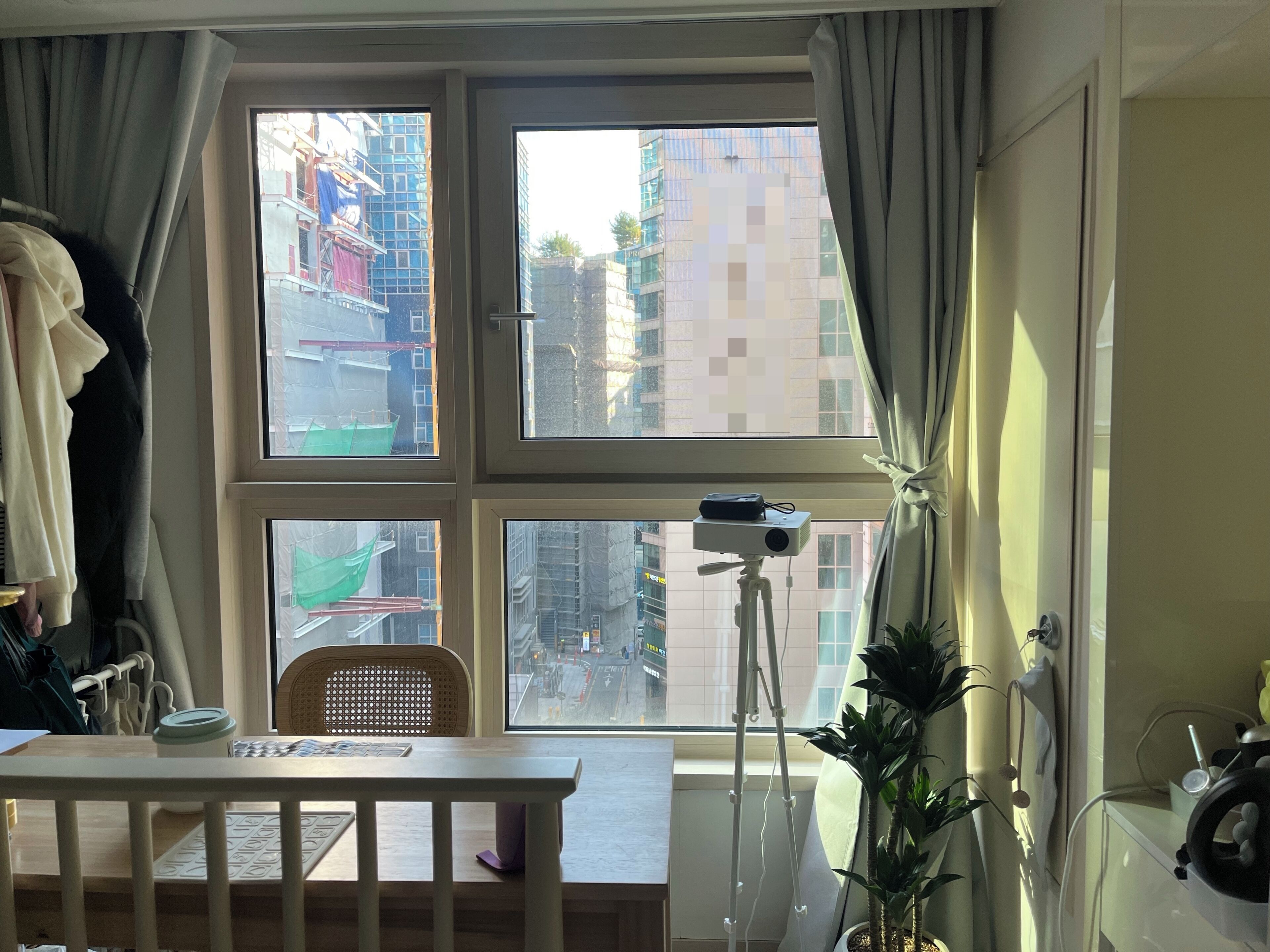 A room with a large window, a desk, a chair, a plant, and a camera on a tripod.