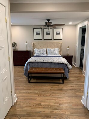 A bedroom with a bed, a bench, a ceiling fan, and framed pictures on the wall.