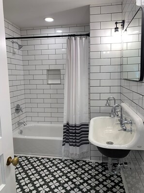 A bathroom with a white bathtub, a white sink, and a shower with a black and white striped shower curtain. The floor has a black and white floral tile pattern.