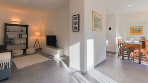 A modern living room with a sofa, ottomans, a TV, and a dining area with a table and chairs.