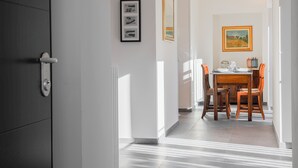 A hallway leading to a dining area with a table and chairs, framed artwork on the walls, and a door with a handle.