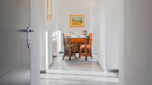 A hallway leading to a dining area with a table and chairs, a framed picture on the wall, and a door on the left.