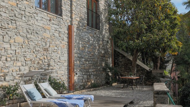 A stone building with lounge chairs and a table outside.