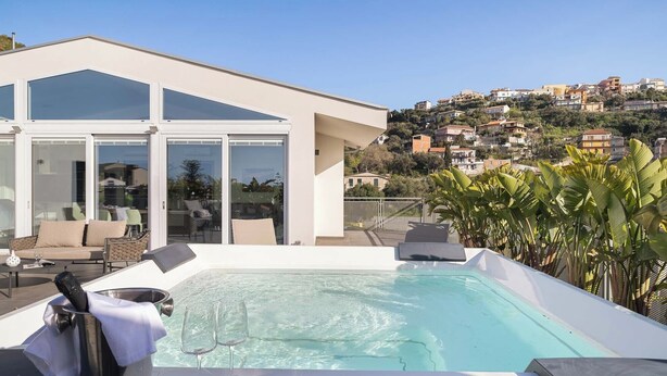 A rooftop pool area with a glass-enclosed lounge, a hot tub, and a view of a hillside town. - Design Apartments D'Orlando (Capo d'Orlando)