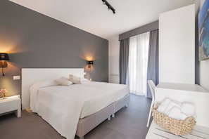 Une chambre à coucher moderne avec un grand lit, des lampes de chevet, une table de chevet avec une lampe, un panier en osier contenant des serviettes et un tableau accroché au mur.