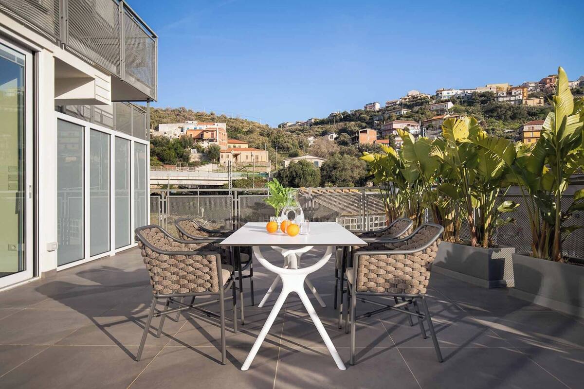 Una terraza con mesa y sillas, vistas a un pueblo en la ladera y una planta en maceta.