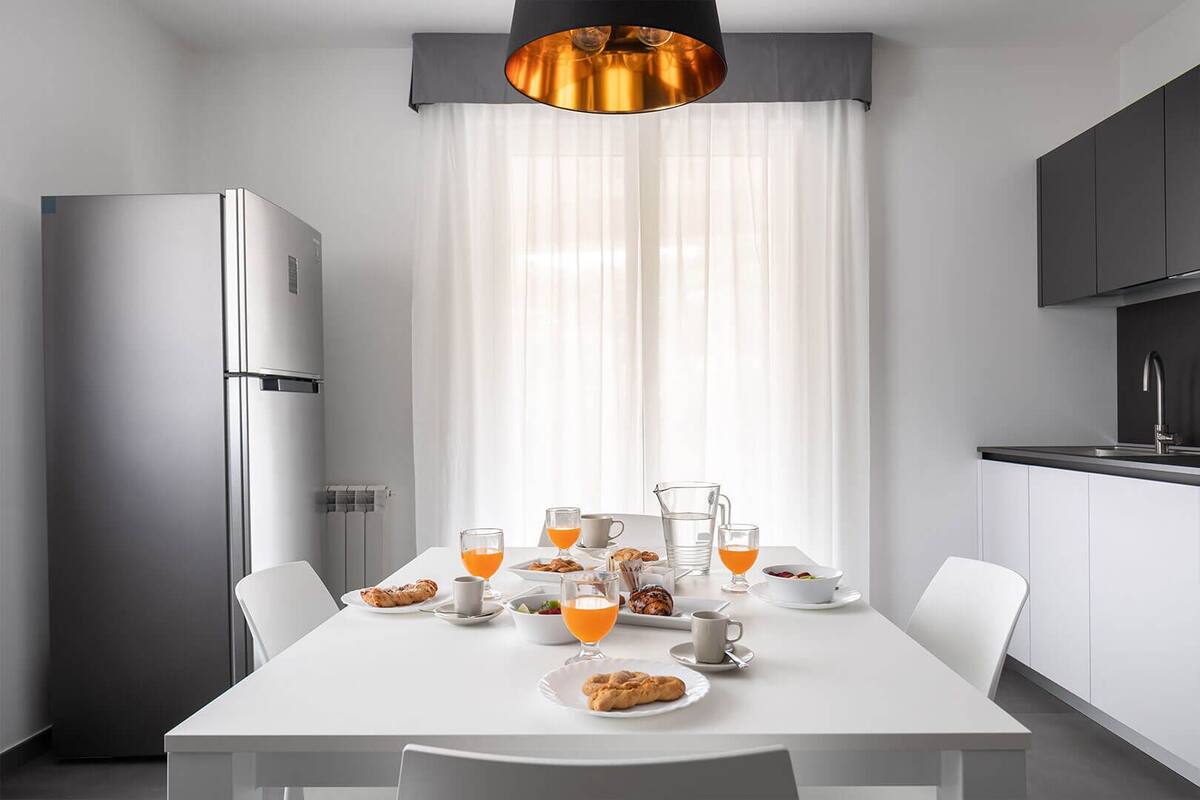 Una cocina moderna con una mesa lista para el desayuno, que incluye cruasanes, zumo de naranja y café.