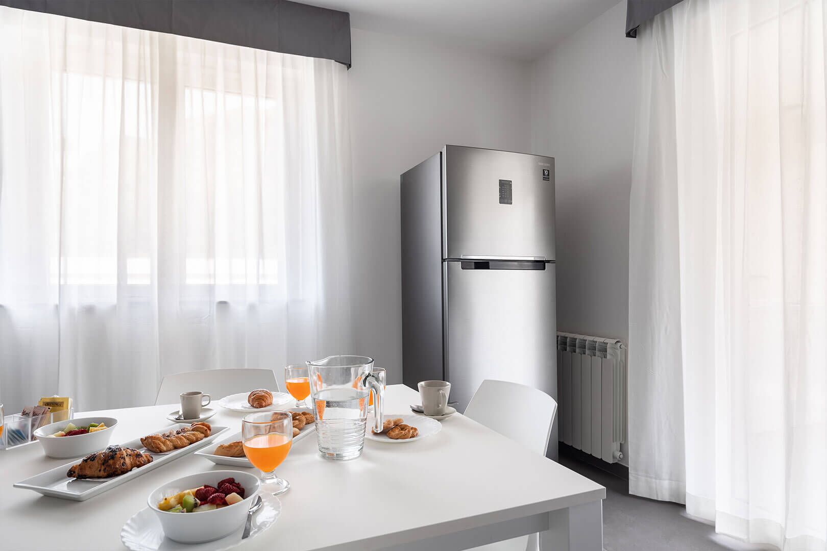A modern hotel room with a dining table set for breakfast, a refrigerator, and a radiator.