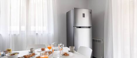 A modern hotel room with a dining table set for breakfast, a refrigerator, and a radiator.