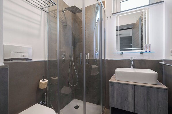 Un baño moderno con ducha envuelta en vidrio, un lavamanos blanco y un espejo sobre él.