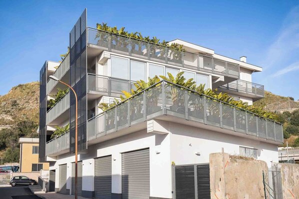 Un immeuble moderne à plusieurs étages, doté de balcons, de grandes portes de garage et surplombant une colline.