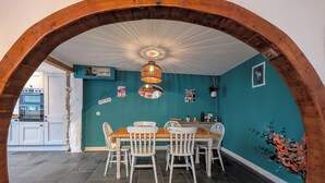 A dining area with a wooden table and chairs, a hanging light fixture, and a teal wall with various decorations. - The Old Barn Near St Ives - Rustic Charm & Space (St Ives)