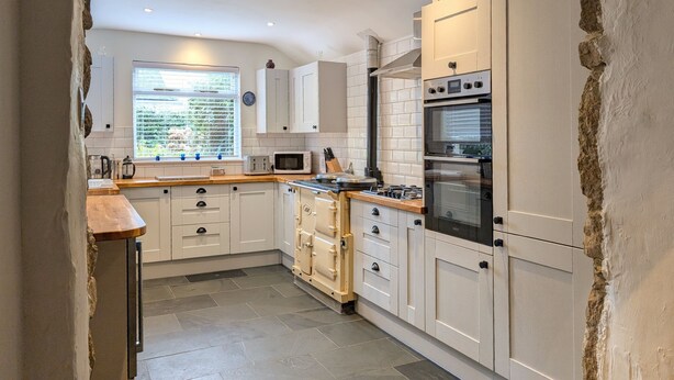 A modern kitchen with white cabinets, a built-in oven, and a window with a view. - The Old Barn Near St Ives - Rustic Charm & Space (St Ives)