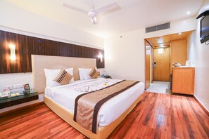 A hotel room with a large bed, wooden flooring, a ceiling fan, a TV, and a small desk with toiletries. - Quality Inn Residency Hyderabad (Hyderabad)