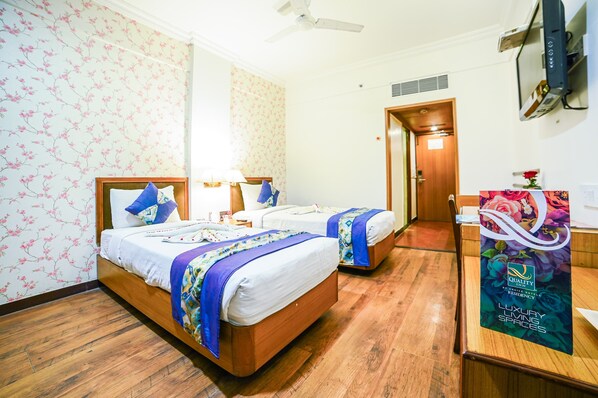 A hotel room with two beds, wooden flooring, floral wallpaper, a ceiling fan, a TV, and a poster advertising the hotel. - Quality Inn Residency Hyderabad (Hyderabad)