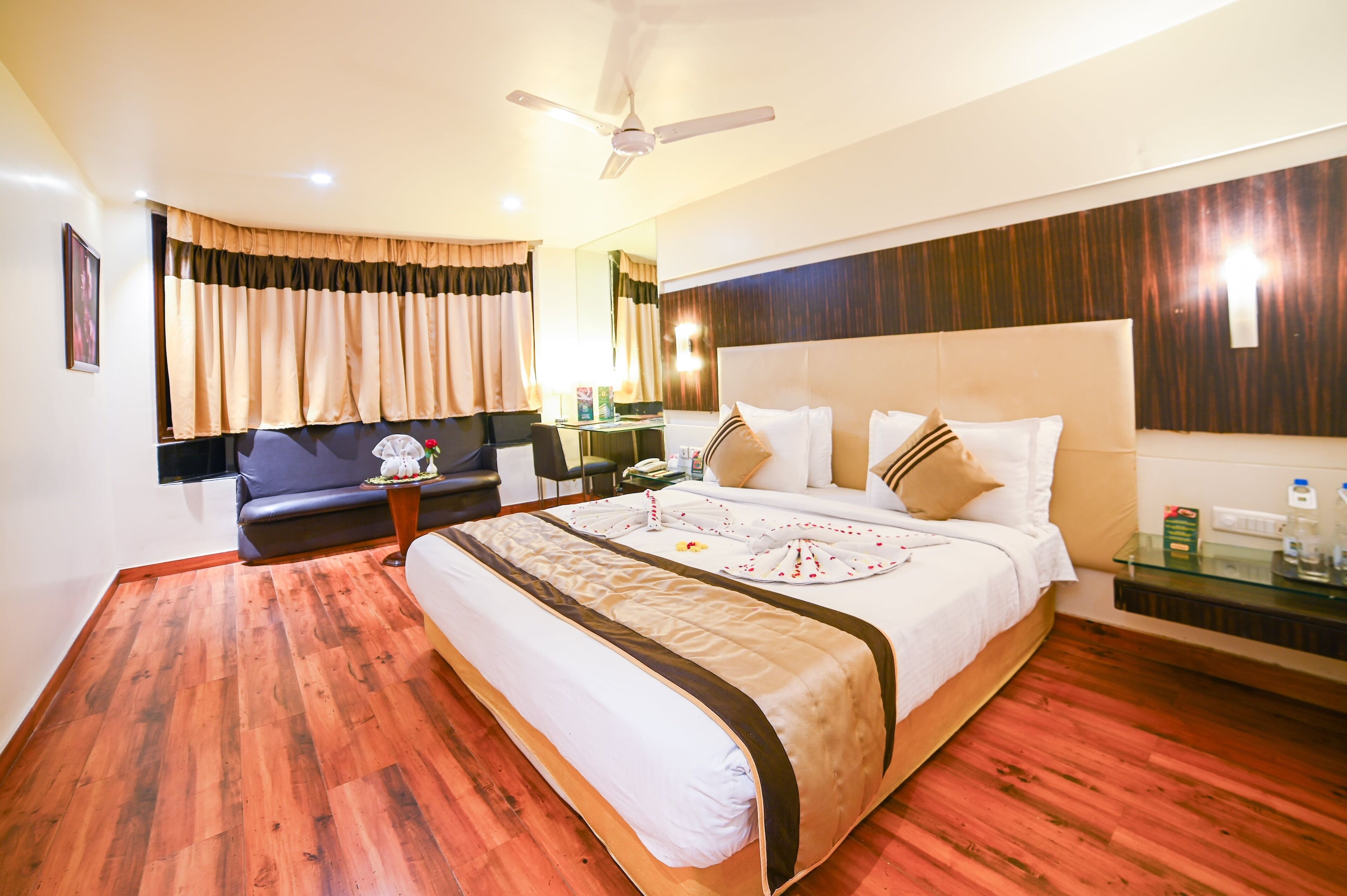 A hotel room with a large bed, a sofa, a desk, and a ceiling fan.