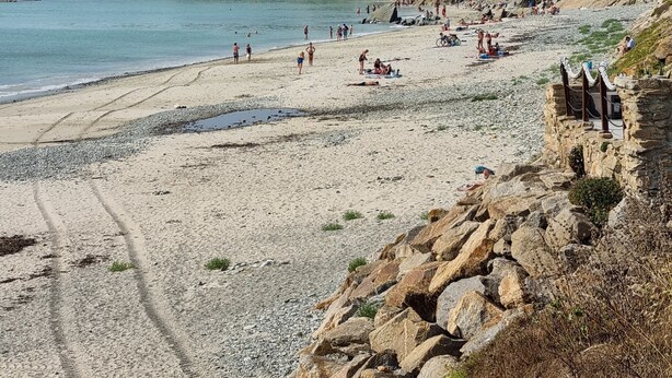 Een strand met mensen, een rotsachtige kustlijn en huizen op de achtergrond.