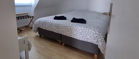 A bedroom with a sloped ceiling, a bed with a floral bedspread, a small wooden bench, and a painting on the wall.