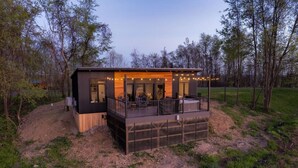 A modern cabin with a wooden deck and large windows, surrounded by trees. - Skyline Serenity | Hot Tub, Panoramic Views, King Bed in PA Wilds (Brookville)