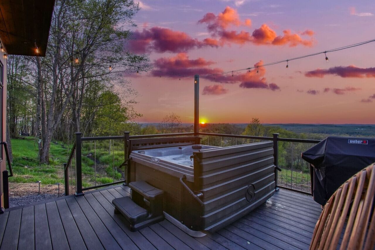 A hot tub on a wooden deck with a view of the sunset and trees.