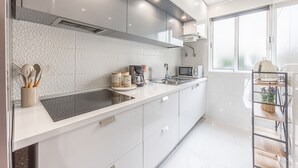 A modern kitchen with a large island, stainless steel appliances, and a view of the outdoors through a large window. - Cozy Seaside Cottage | Ocean Views & Near Beach (Caniço)