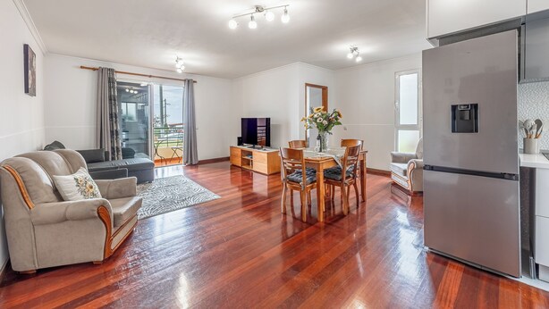 A spacious living area with a wooden floor, a sofa, a dining table with chairs, a flat-screen TV, and a refrigerator. - Cozy Seaside Cottage | Ocean Views & Near Beach (Caniço)