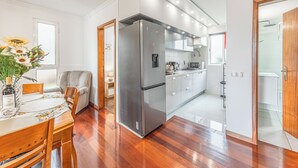 A modern kitchen with a refrigerator, a dining area with a table and chairs, and a view into the adjacent bathroom. - Cozy Seaside Cottage | Ocean Views & Near Beach (Caniço)
