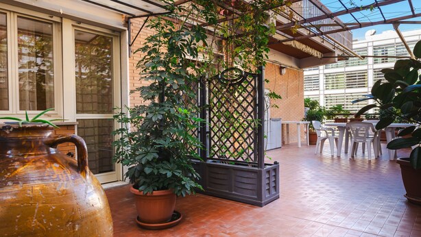 Un espace extérieur aménagé en terrasse, avec des carreaux de terre cuite, des plantes en pot et un grand vase.
