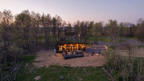 Une cabane moderne dotée d’une terrasse et de mobilier d’extérieur, entourée d’arbres et bordée d’un sentier de terre.
