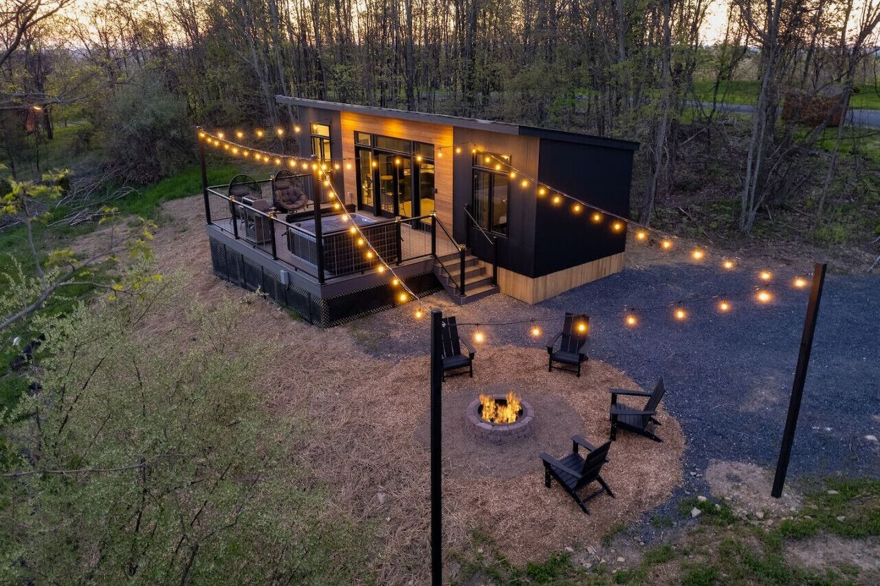 Una cabaña moderna con terraza, asientos exteriores y una fogata.