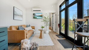 Un salon moderne avec un canapé en cuir, une petite table d’appoint ornée d’une plante et une grande fenêtre donnant sur l’extérieur.