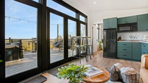 Une cuisine moderne dotée de grandes fenêtres, un coin repas avec des chaises et une terrasse en bois visible à travers les fenêtres.