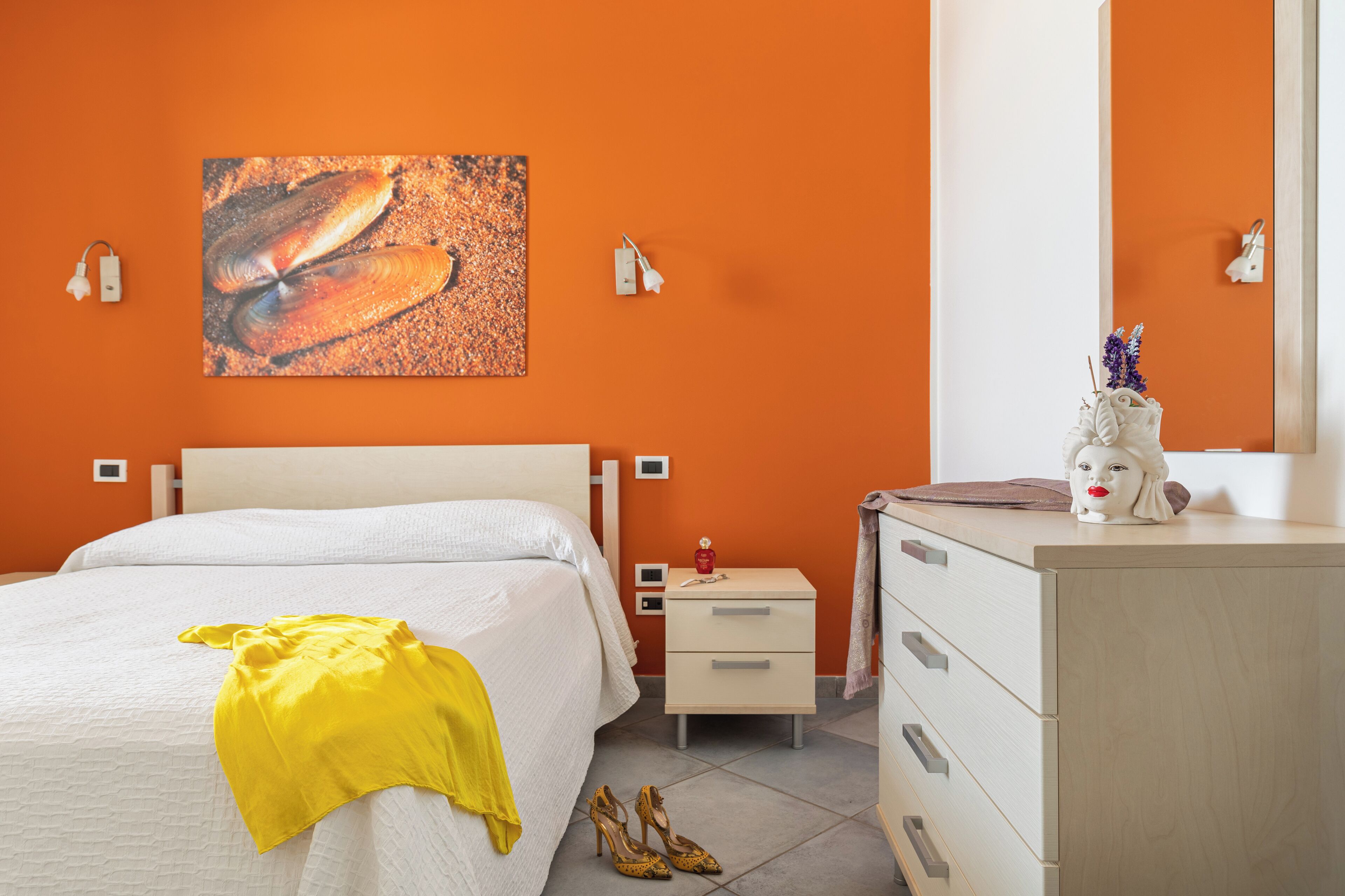 Habitación de hotel con una cama, una mesita de noche, un aparador y una pared naranja.