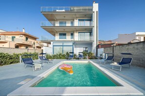 A modern multi-story building with a swimming pool, lounge chairs, and a decorative float. - Terraces d'Orlando (Capo d'Orlando)