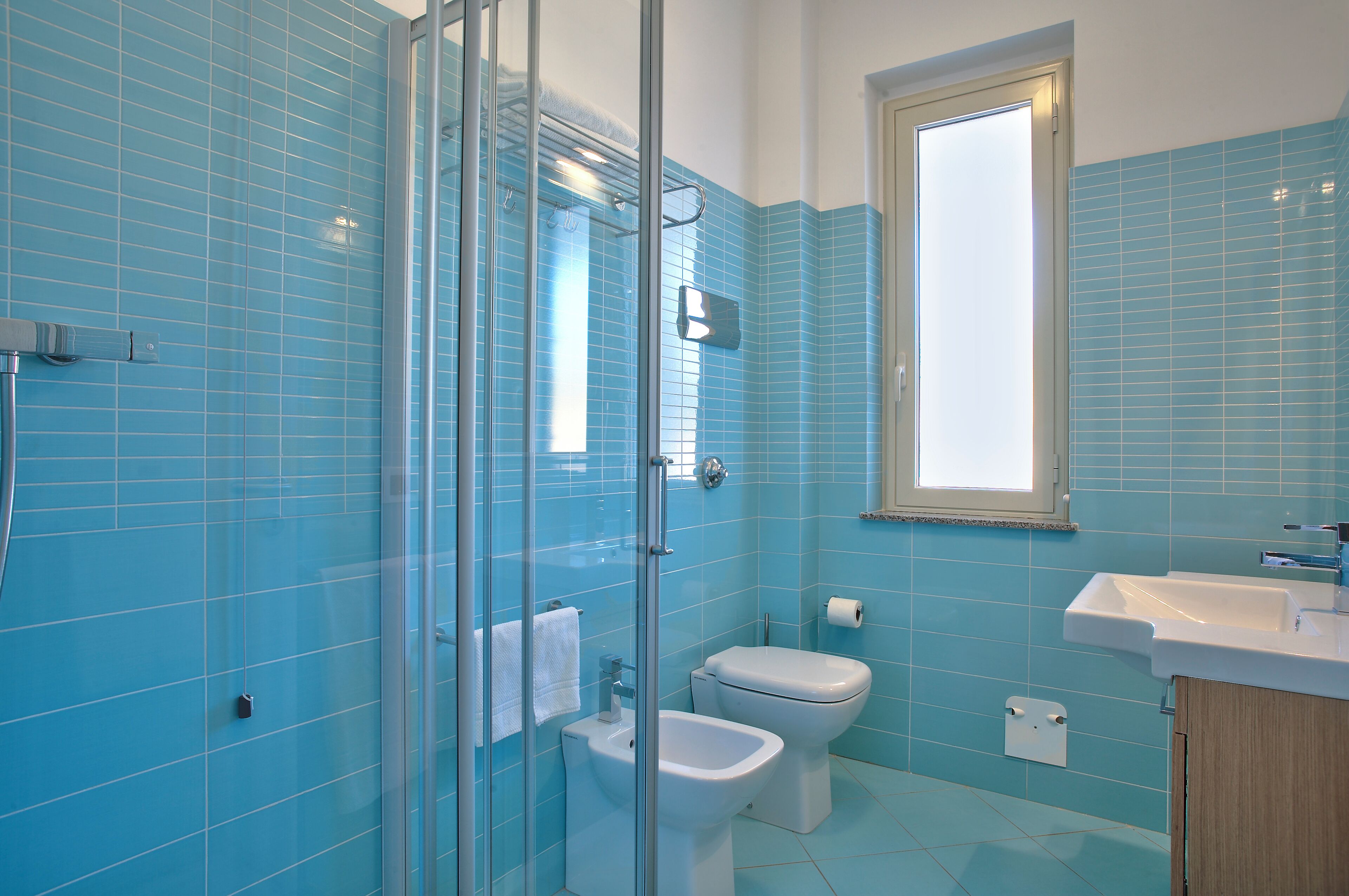 A bathroom with blue tiles, a glass shower enclosure, a toilet, and a sink.