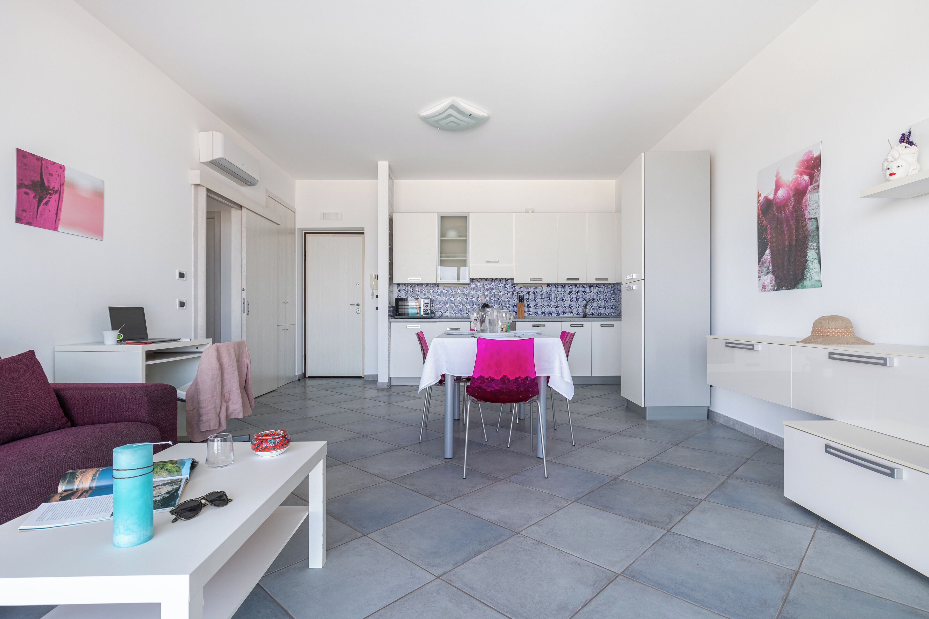 Una sala de estar moderna con comedor, muebles blancos y una cocina al fondo.
