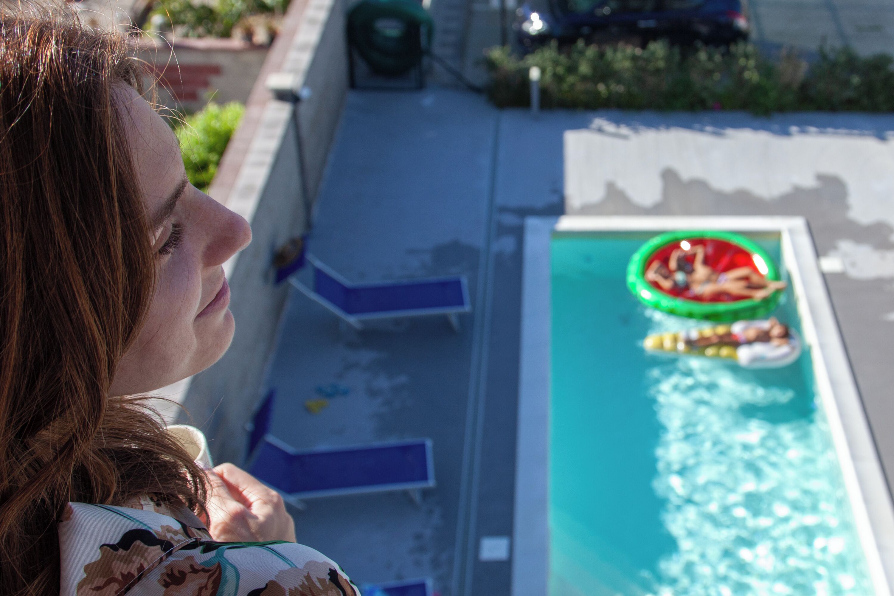 Une piscine avec des chaises longues et un objet circulaire vert flottant à la surface de l’eau.