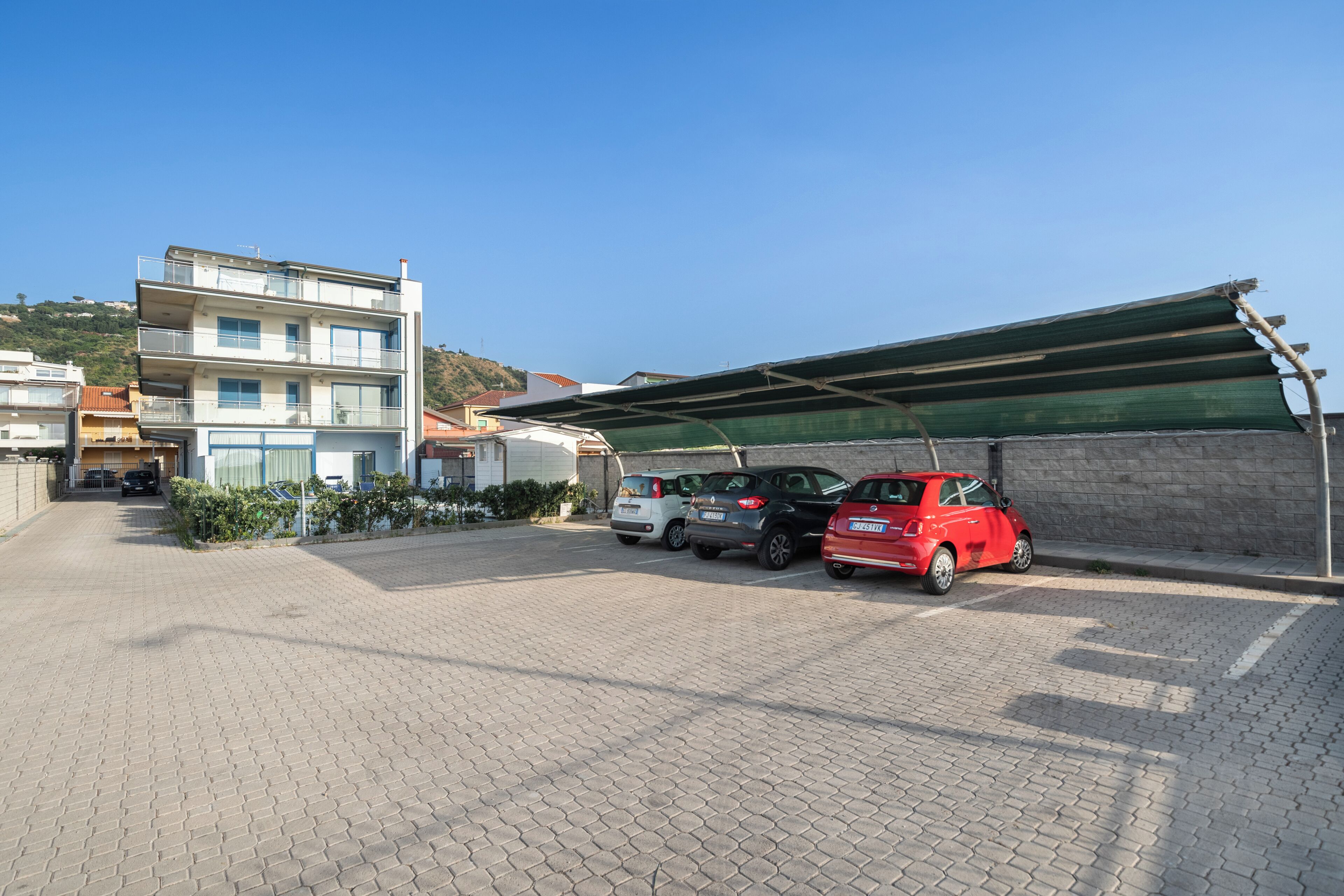 A parking area with a building in the background, a covered carport, and a clear sky.