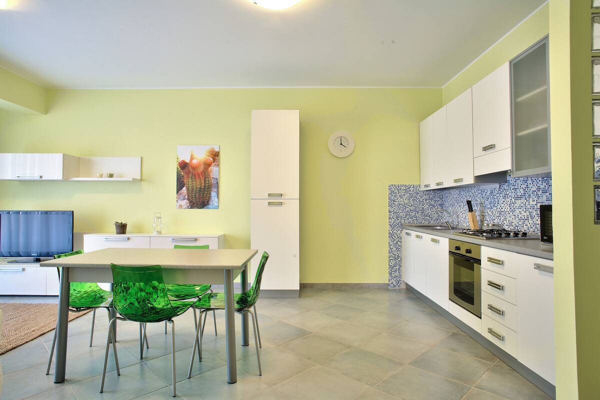 Une cuisine moderne avec des meubles blancs, un pare-feu en carrelage et un coin repas avec des chaises vertes.