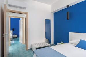A modern hotel room with a large bed, a bedside table, a nightstand, a wall-mounted air conditioner, and a bathroom visible through an open door. - Terraces d'Orlando (Capo d'Orlando)