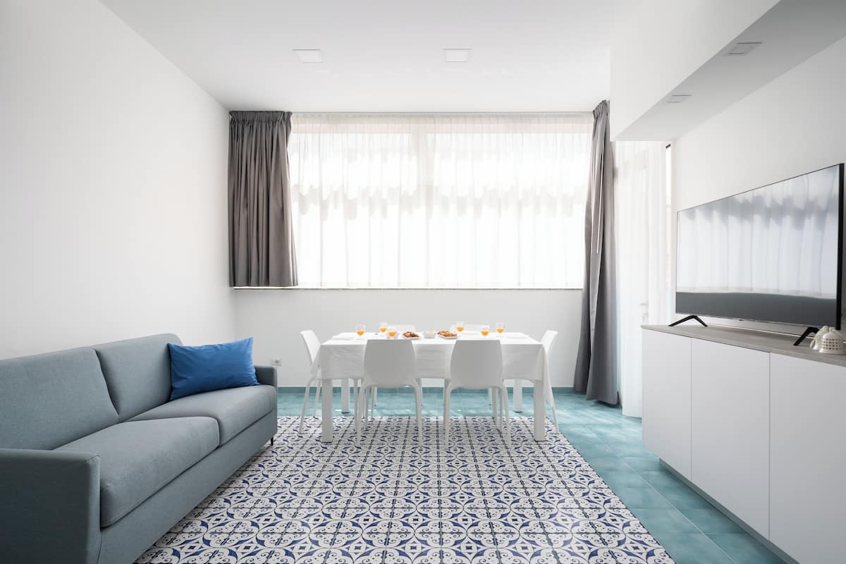 Un salon moderne avec un canapé gris, une table à manger avec des chaises, un téléviseur posé sur un meuble et un tapis à motifs.