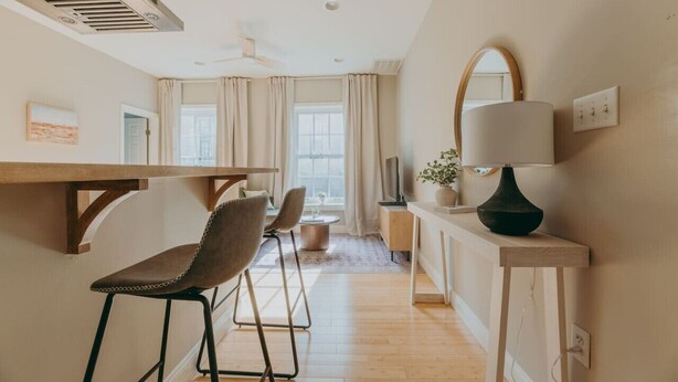 A modern kitchen with a wooden table, two chairs, a ceiling fan, and a large window with curtains. - The Maisonette on Duke | King Bed, Chic, Downtown Lancaster (Lancaster)
