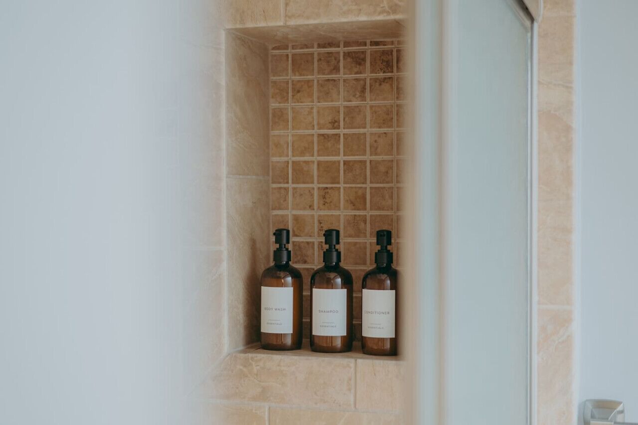 Et badeværelse med flisebelagt brusevæg og tre flasker sæbe, shampoo og balsam.