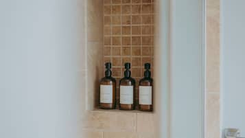Et badeværelse med flisebelagt brusevæg og tre flasker sæbe, shampoo og balsam.