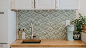 A kitchen with white cabinets, a green tiled backsplash, a stainless steel faucet, a sink, and a coffee maker on the counter. - The Maisonette on Duke | King Bed, Chic, Downtown Lancaster (Lancaster)