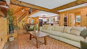 A spacious living area with a wooden staircase, a sofa, a coffee table, and a dining area.