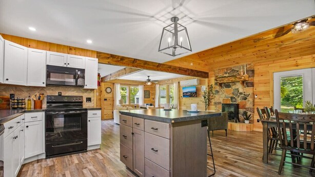 A spacious kitchen with wooden beams, a central island, and a stone fireplace.