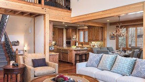 A spacious living area with a high ceiling, wooden beams, a staircase, and a kitchen with wooden cabinets and a dining area. - Hot Tub + Close to Skiing – Lariat Ridge Lodge (Steamboat Springs)