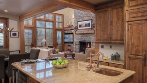 A spacious kitchen with a stone fireplace, wooden cabinets, and a large window with blinds. - Hot Tub + Close to Skiing – Lariat Ridge Lodge (Steamboat Springs)