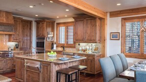 A spacious kitchen with wooden cabinets, a large island, and a dining area with a table set for two. - Hot Tub + Close to Skiing – Lariat Ridge Lodge (Steamboat Springs)